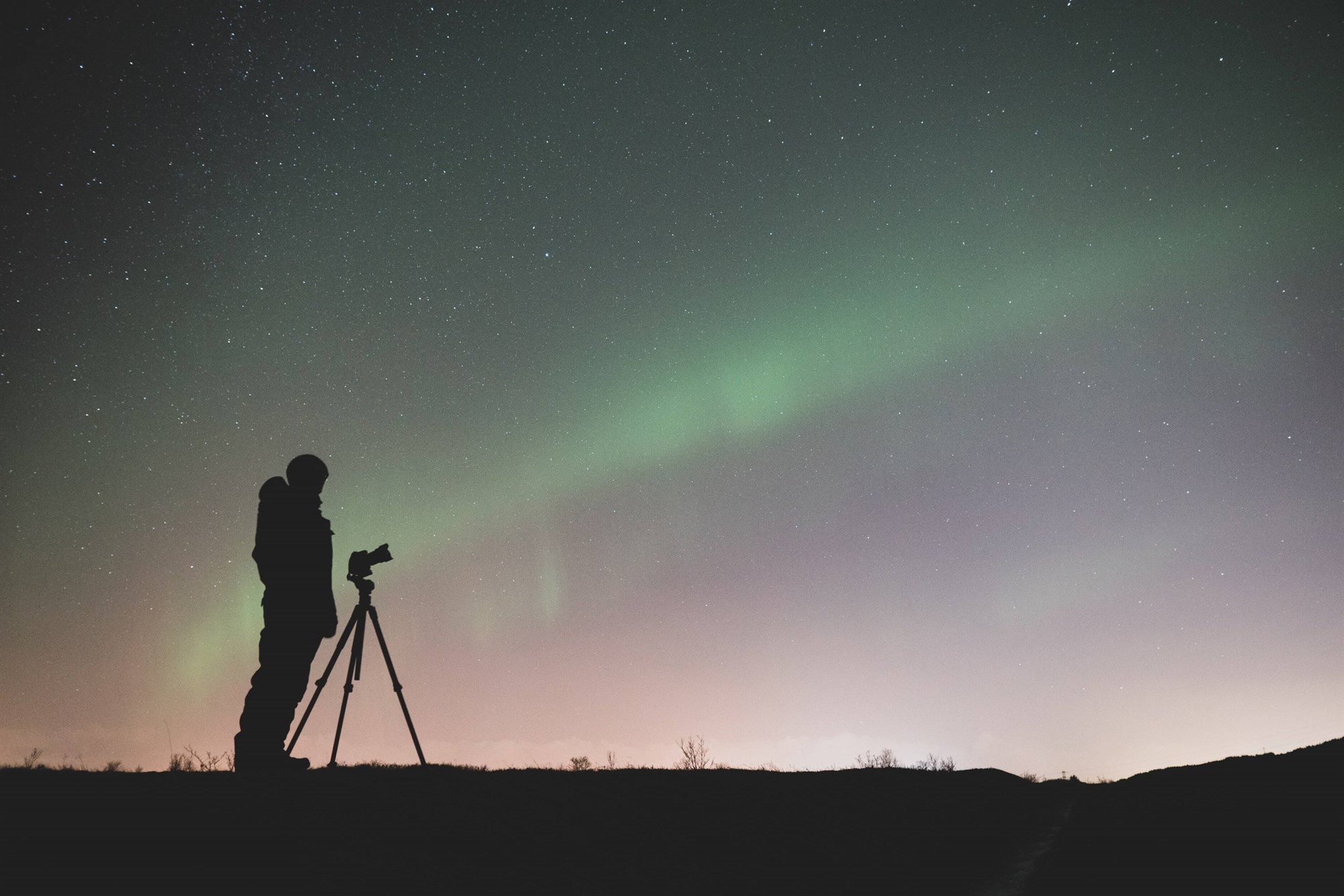 Silhouette of a person with a camera underneath the Northern Lights